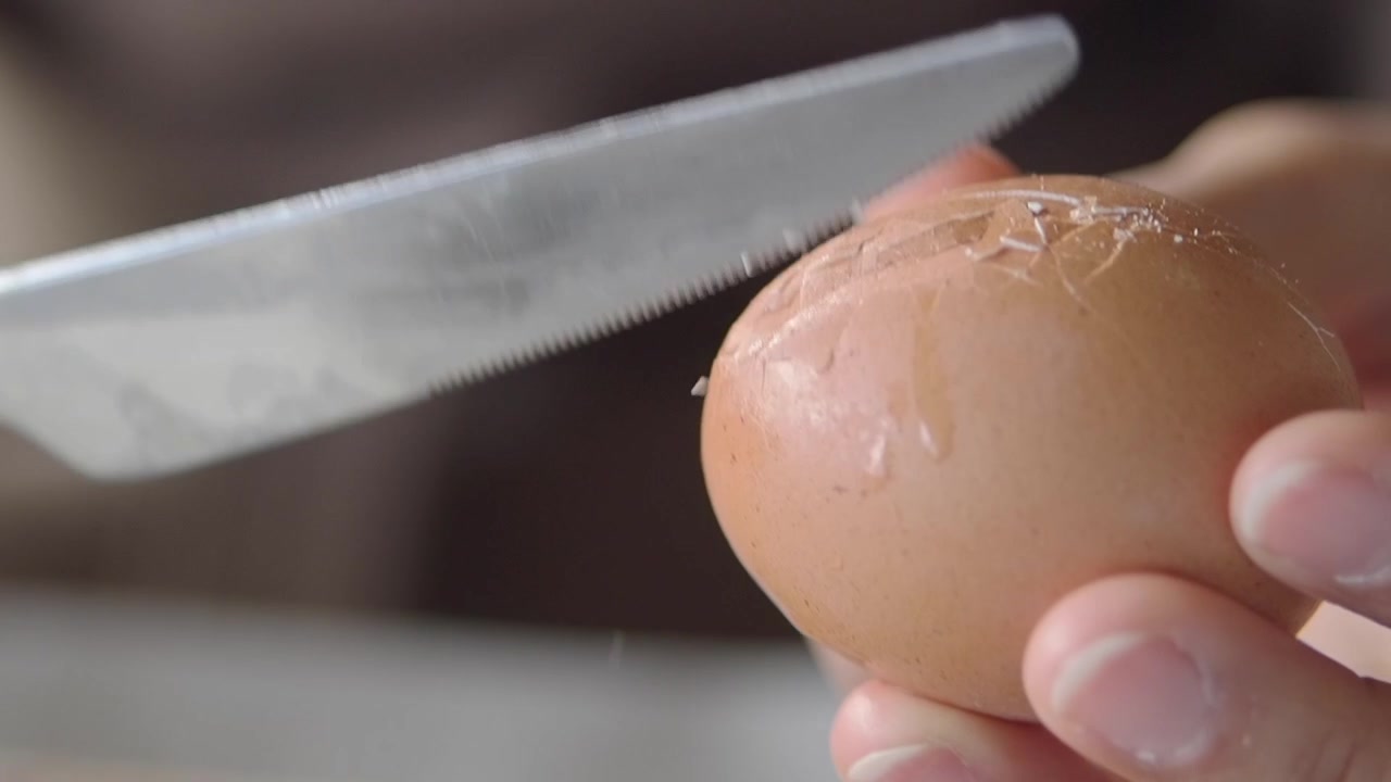 Close-Up of Hand Cracking a Brown Egg with a Knife