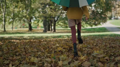 rear view and tilt up of caucasian girl walking across the park with colorful umbrella.