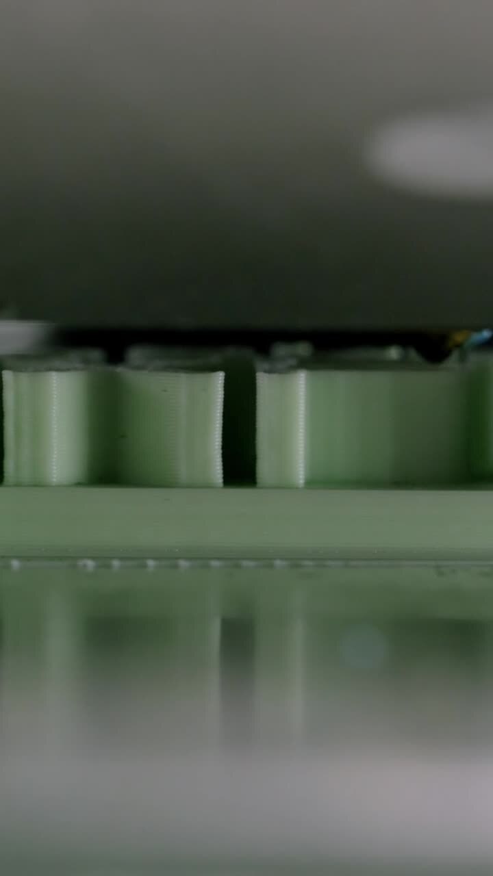 Primo piano di una stampante 3D che estrude filamento di plastica verde strato dopo strato