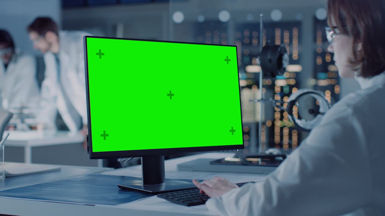 여성 it 과학자는 녹색 모형 화면 컴퓨터를 사용합니다. 배경에는 과학자, 엔지니어와 함께 하이테크 디자인을하는 기술 연구 및 개발 실험실이 있습니다.