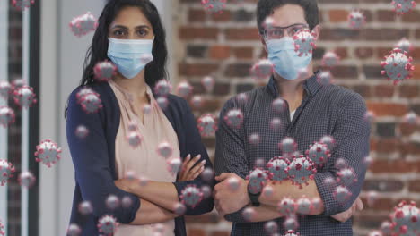 animation of covid 19 cells floating over portrait of man and woman wearing face masks in office