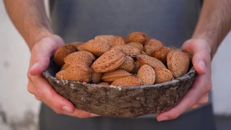 hombre sosteniendo un tazón de nueces de almendras con cáscara
