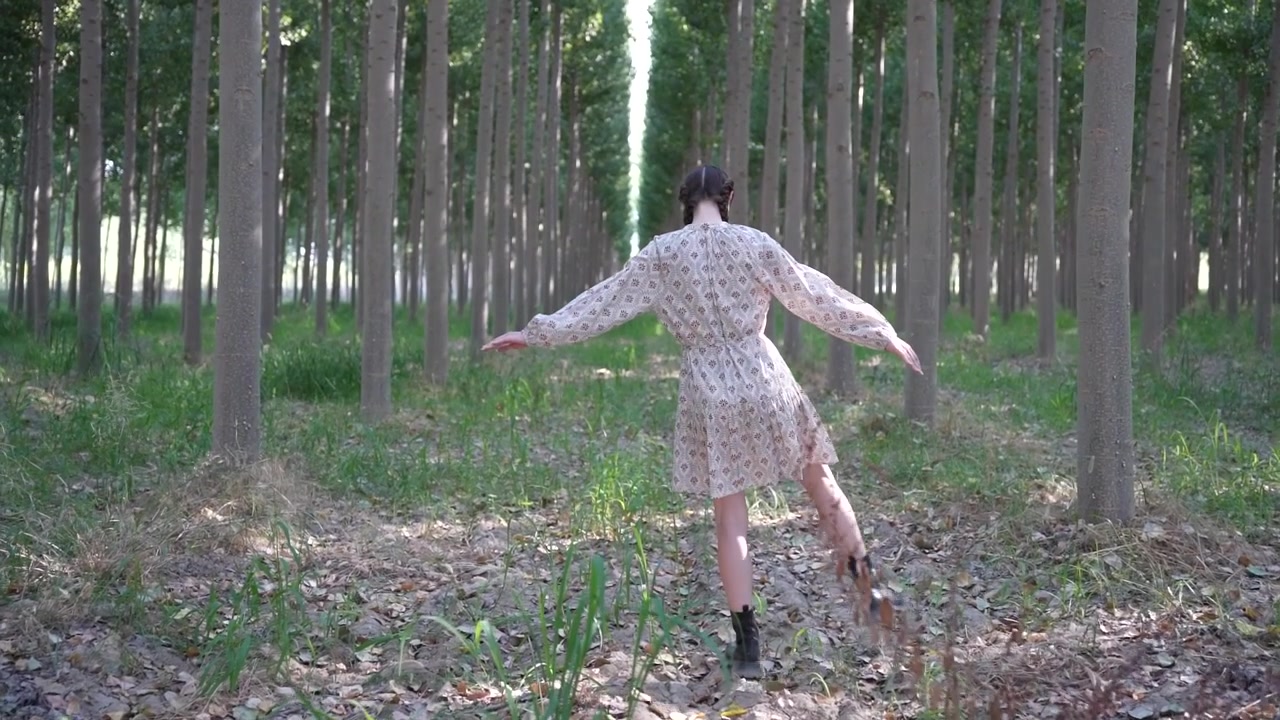 A young woman strolling along a scenic forest path enveloped by majestic tall trees