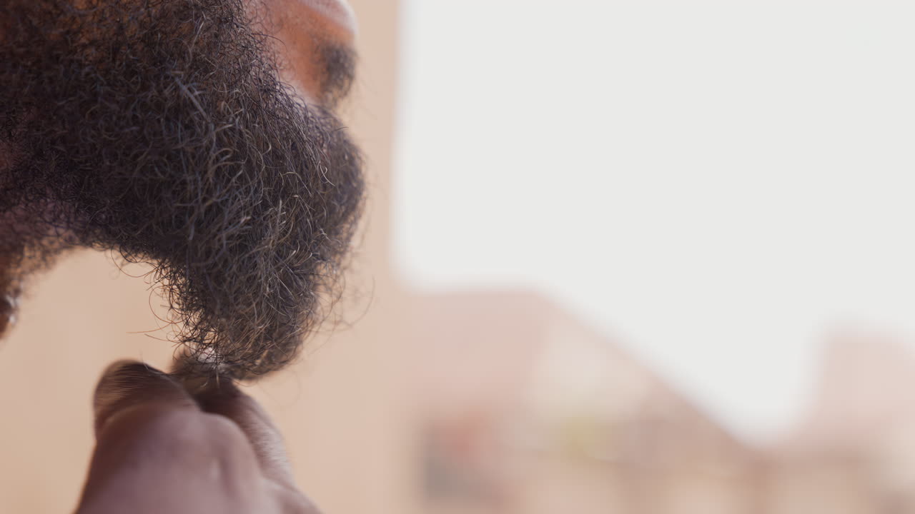 Primo piano di una mano con barba nera che accarezza il mento in una luce urbana soffusa, consistenza ruvida dei peli e dita che seguono la mascella, dettaglio di un ritratto intimo che mostra labbra e profilo, rituale pre-partita silenzioso e concentrato.