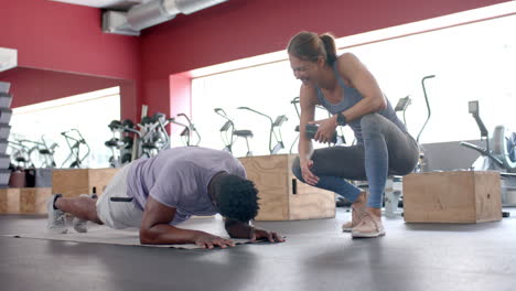hombre afroamericano en forma hace una tabla en el gimnasio con entrenador, con espacio de copia