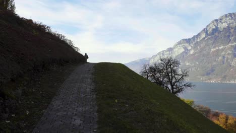 dolly shot to a woman who is walking on top of a hill next to a lake