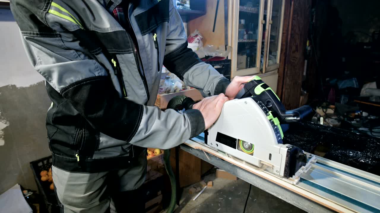 회색 오버을 입은 수염을 가진 젊은 남자가 직업으로 목수입니다. 원형 절단 기계로 일합니다.