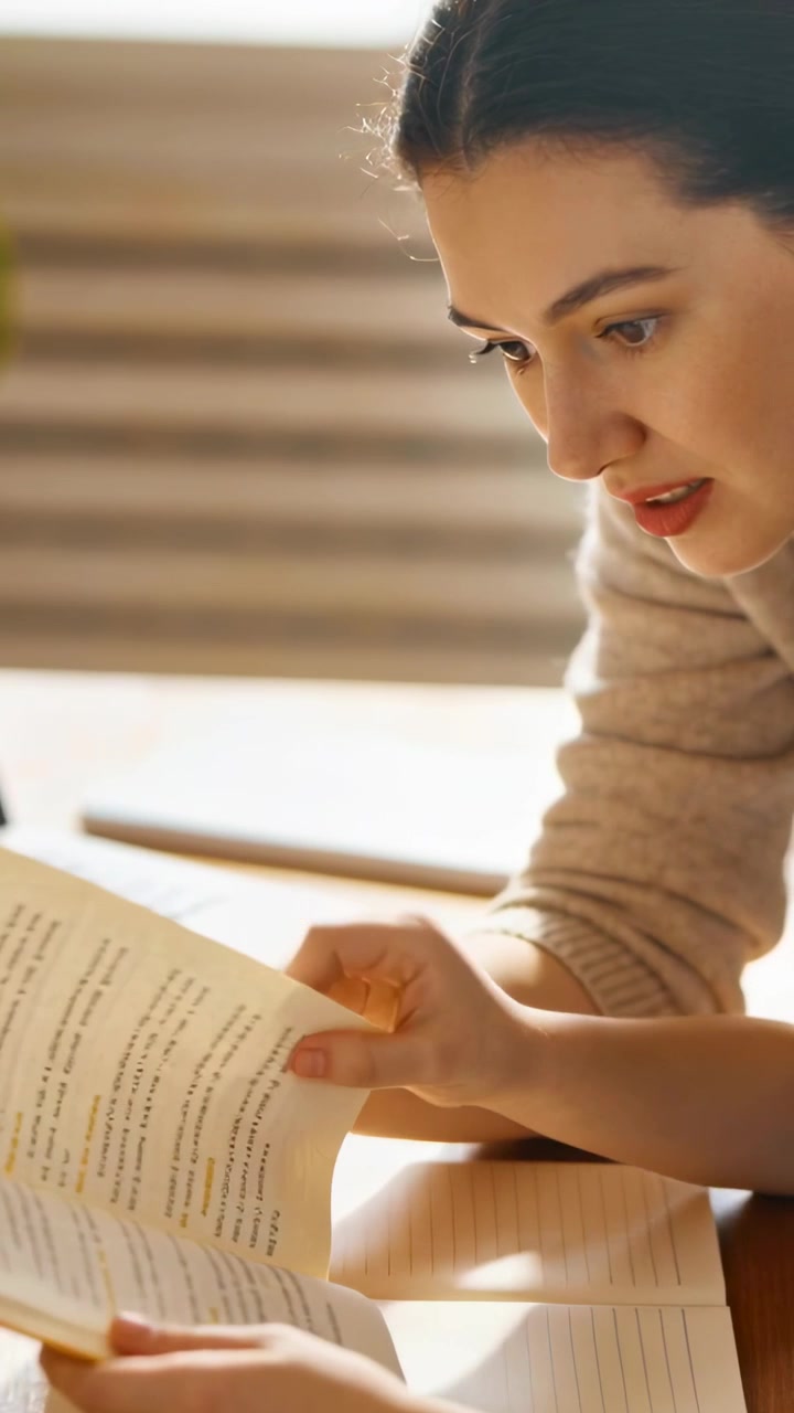 Vertical video: Pointing at line woman in tan top tracing open book, turning page at home studying