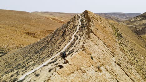 Dramatische-Drohnenaufnahme-Eines-Wanderers-In-Der-Wüste,-Der-Entlang-Eines-Hohen-Grats-Mit-Blick-Auf-Einen-Spektakulären-Berg-Und-Krater-Geht