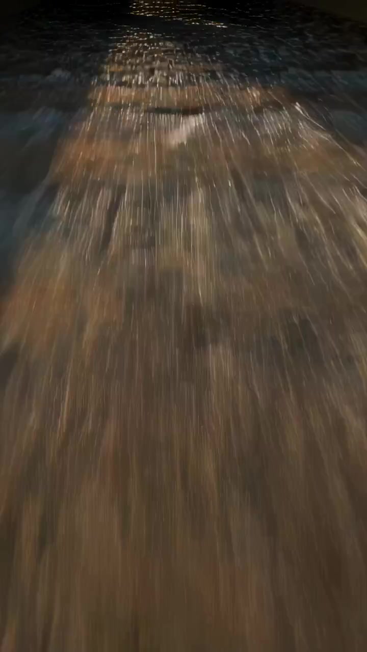 Video verticale: Marea che spinge acqua a velo su gradini bagnati di un molo, riflettendo luci.