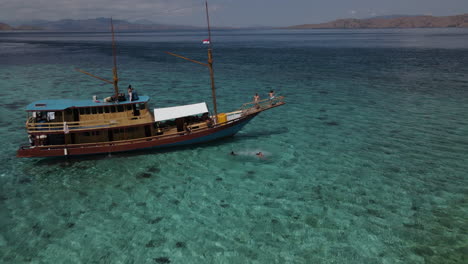 wooden boat floating near the rocky shore with white sand in the island of labuan bajo in flores, indonesia at summer. drone shot
