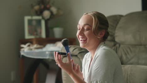 young woman in pajamas playfully applies makeup by window, smiling and laughing