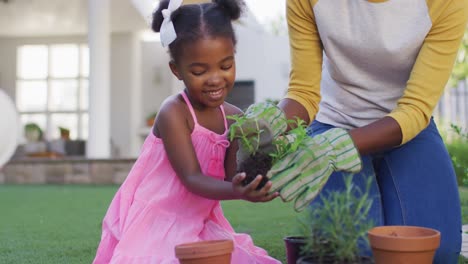 happy african american mother and daughter gardening, planting plants in garden