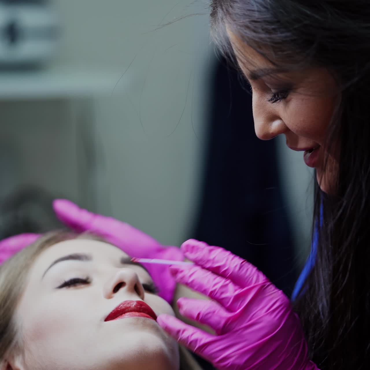 Beautician doing permanent makeup on lips. Skilled cosmetologist woman applying cosmetic procedure on patient's lips in modern spa salon.