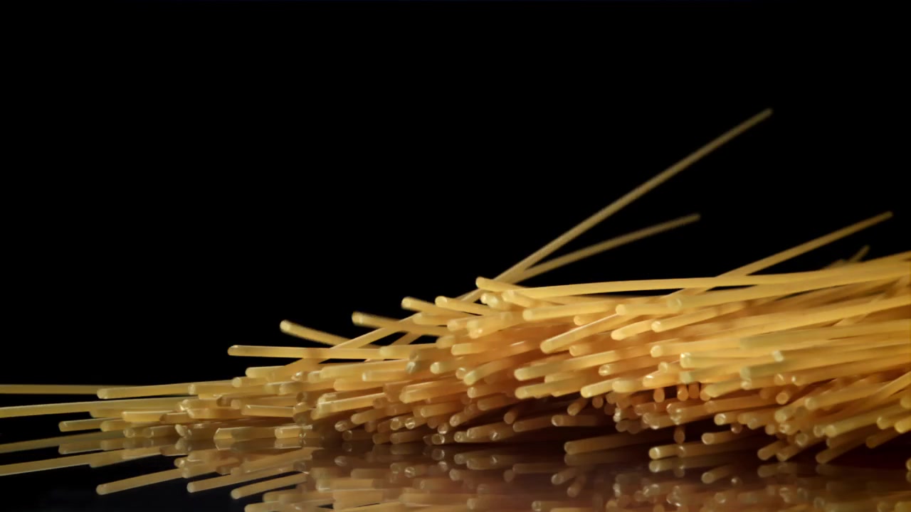 Spaghetti secchi che cadono al rallentatore su una superficie nera riflettente.