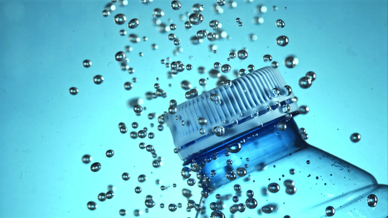 Primo piano di una bottiglia d'acqua di plastica con bolle che salgono in liquido blu