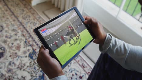 Zusammensetzung-Eines-Mannes,-Der-Zu-Hause-Sitzt-Und-Sich-Ein-Rugbyspiel-Auf-Einem-Tablet-Anschaut