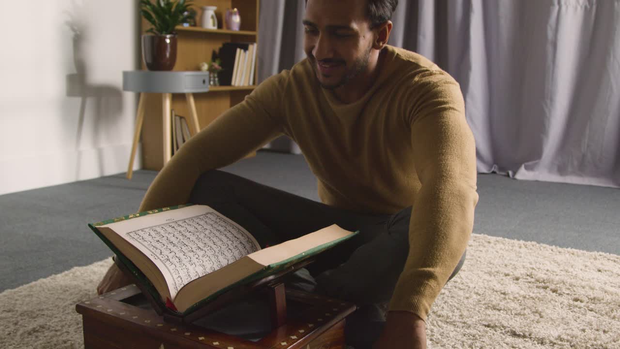 Muslim Man At Home Sitting On Floor And Reciting From The Quran