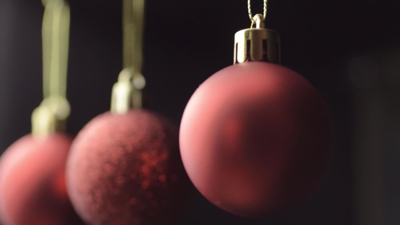 Close-up de três enfeites de Natal vermelhos pendurados em um fundo preto