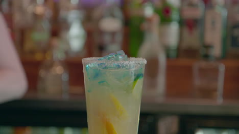 margarita cocktail being poured into tall glass with ice and lemons