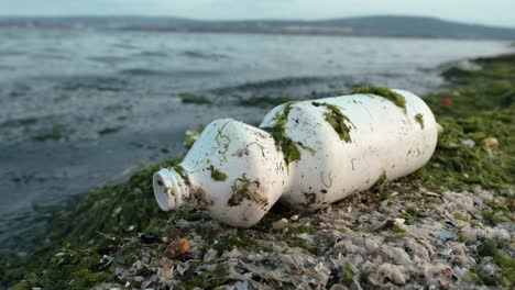 basura derramada en la playa de una gran ciudad. botella de plástico sucia usada vacía. mar sucio, costa arenosa del mar negro. contaminación ambiental. problema ecológico. bokeh de olas en movimiento en el fondo