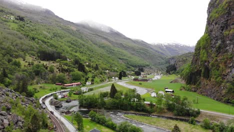 Aerial:-Flåm-train-going-through-a-valley-among-green-meadows