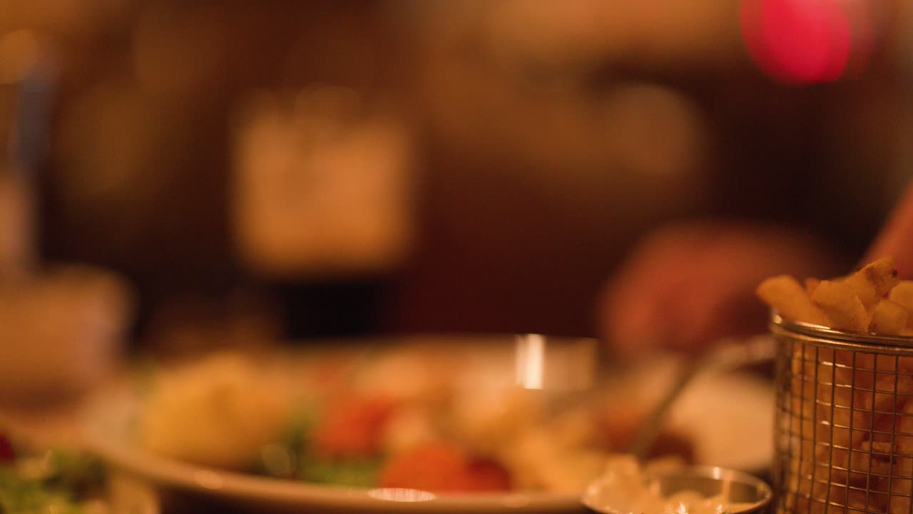 Warmly lit restaurant scene with hand reaching for fries, shallow depth of field, soft focus