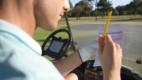 Golfer-sitting-in-golf-buggy-writing-on-paper