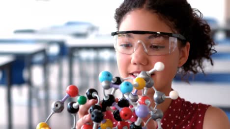 attentive schoolgirl experimenting molecule model in laboratory