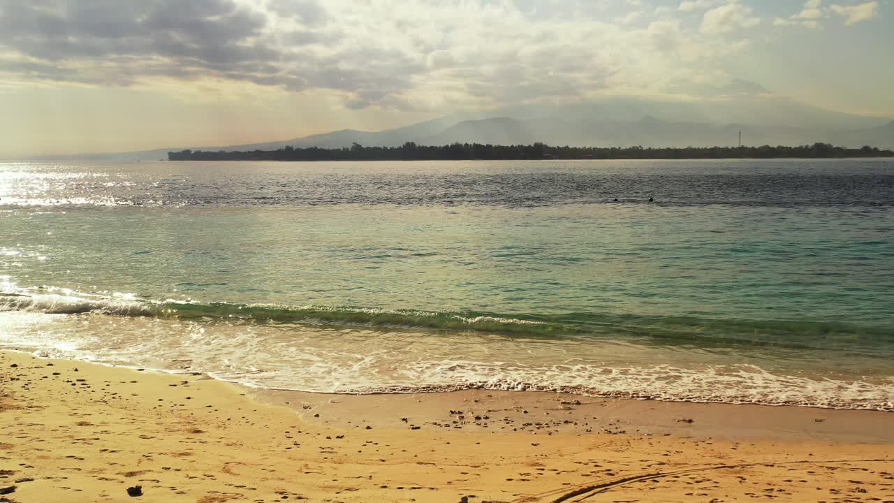 espectacular paisaje marino con nubes grises ocultando el sol al atardecer reflejando en la tranquila laguna con olas salpicando en la playa de arena, bali