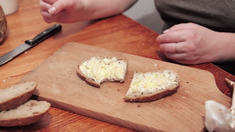 Woman's hands take a cut slice of bread smeared with butter and garlic on a cutting board