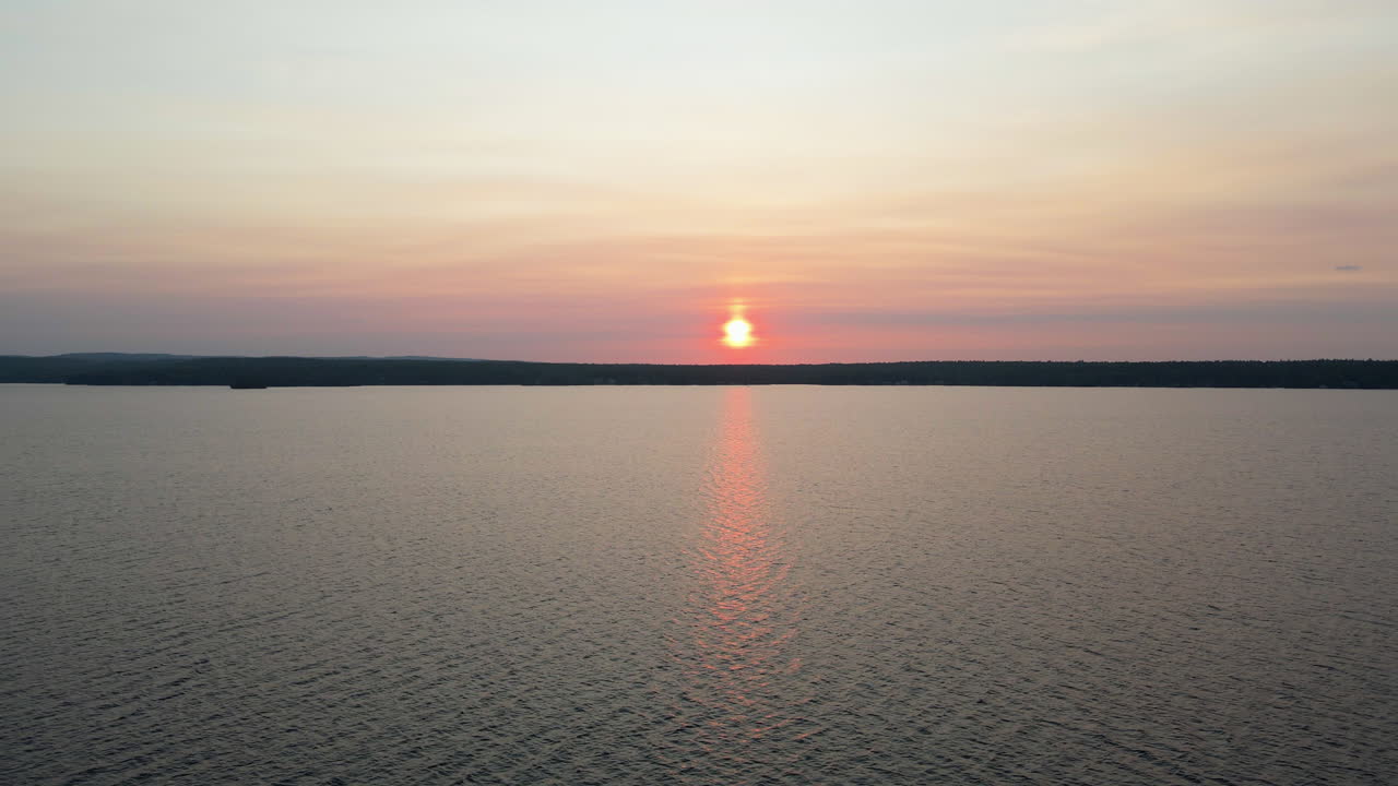 Aerial footage of orange sunset over calm lake with green tree covered hills in the background. Calabogie Ontario