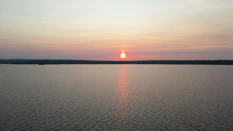 aerial footage of orange sunset over calm lake with green tree covered hills in the background. calabogie ontario