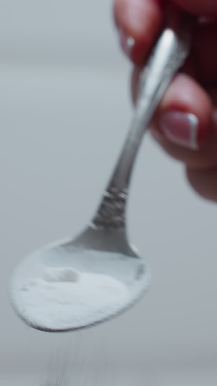 primer plano de la cuchara en la mano mientras el azúcar se vierte gradualmente con un fondo azulejoso brillante, las partículas finas de azúcar caen delicadamente, creando un momento culinario suave en un entorno de cocina bien iluminado