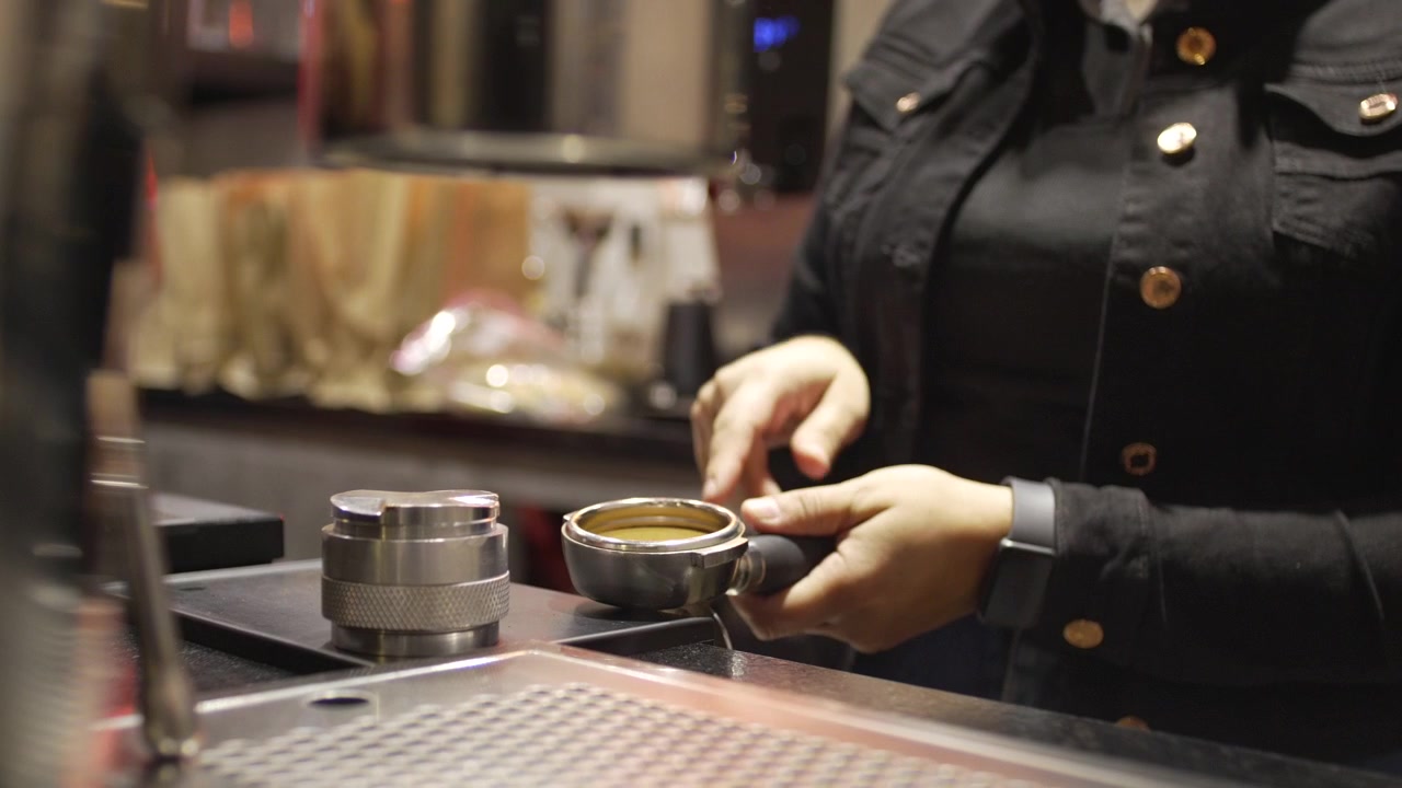 Primo piano di barista che pressa il pressino del caffè nel portafiltro al bancone di un caffè professionale specializzato