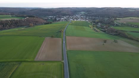 a long country road leading through differently coloured fields and meadows in hesse, germany at sunset