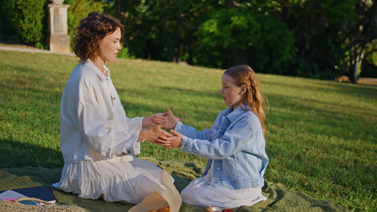 Carefree mother child clapping hands at green grass picnic. Mom daughter playing