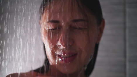 smiling woman under pouring water in shower closeup. relaxed lady enjoys spa procedures standing in bathroom. recreation and hygienic routine