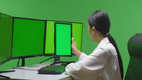 woman working on a tablet with green screen and multiple monitors