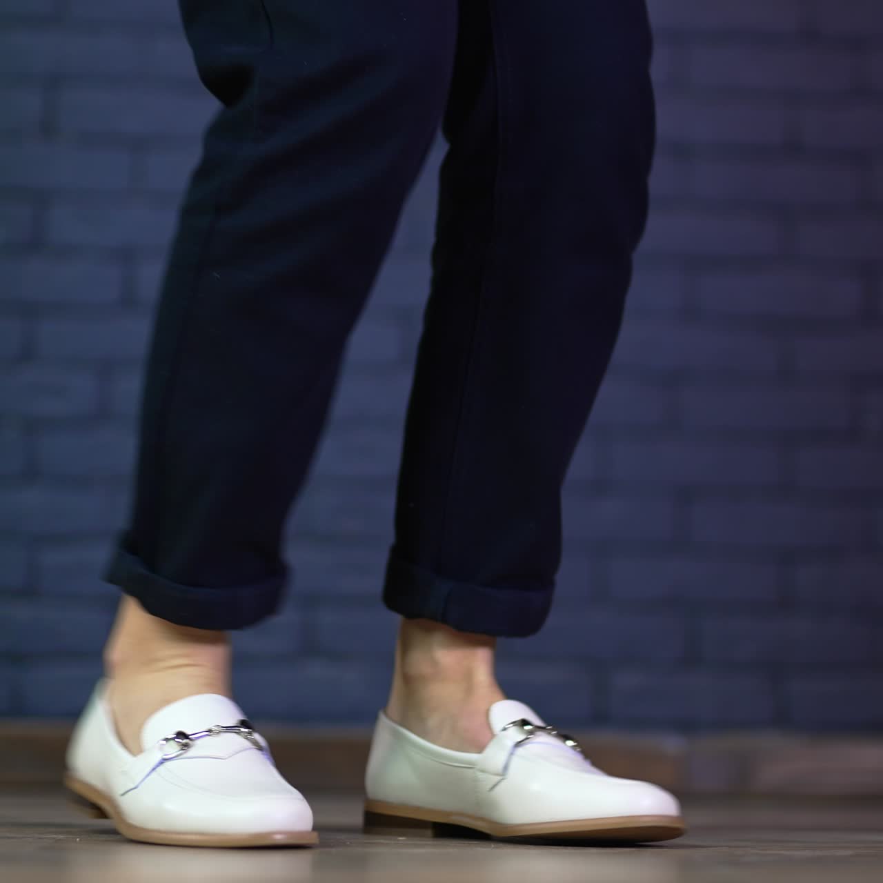 White shoes demonstration on a model. Female feet twisting back and forth in new comfortable footwear. Blue brick backdrop