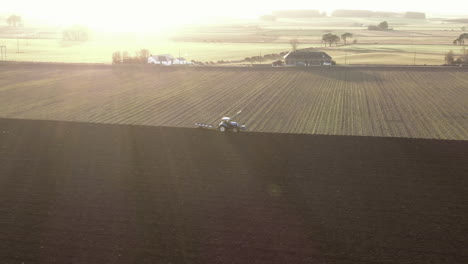 Aerial-view-of-a-farm-tractor-ploughing-a-field-in-Aberdeenshire-on-a-sunny-day,-Scotland