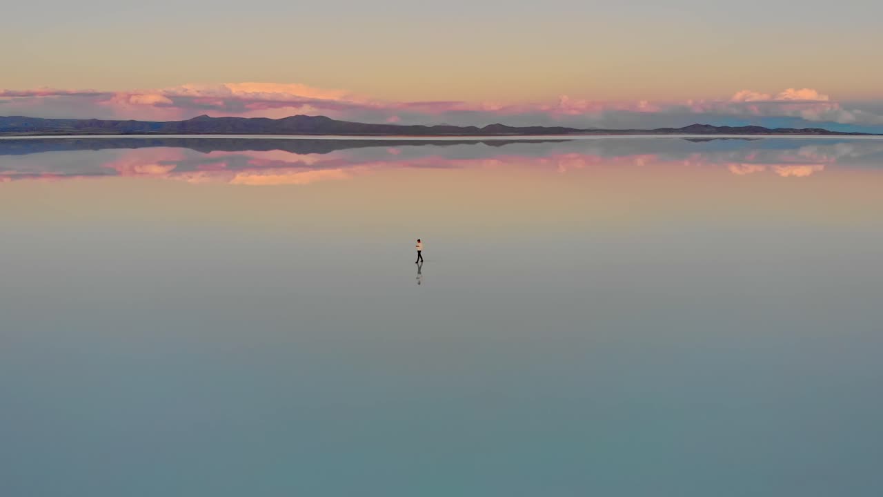 Aerial of a lone figure standing on the mirrored reflection of the world's largest salt flat at dusk in Uyuni Salt Flats , Bolivia