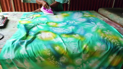 aprendiendo batik casero, sarong, pareo, hombre de piel oscura planchando pintura seca para sellar mahe seychelles 25fps 7
