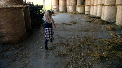 vista posteriore della bambina caucasica che corre in una stalla con scorte di fieno