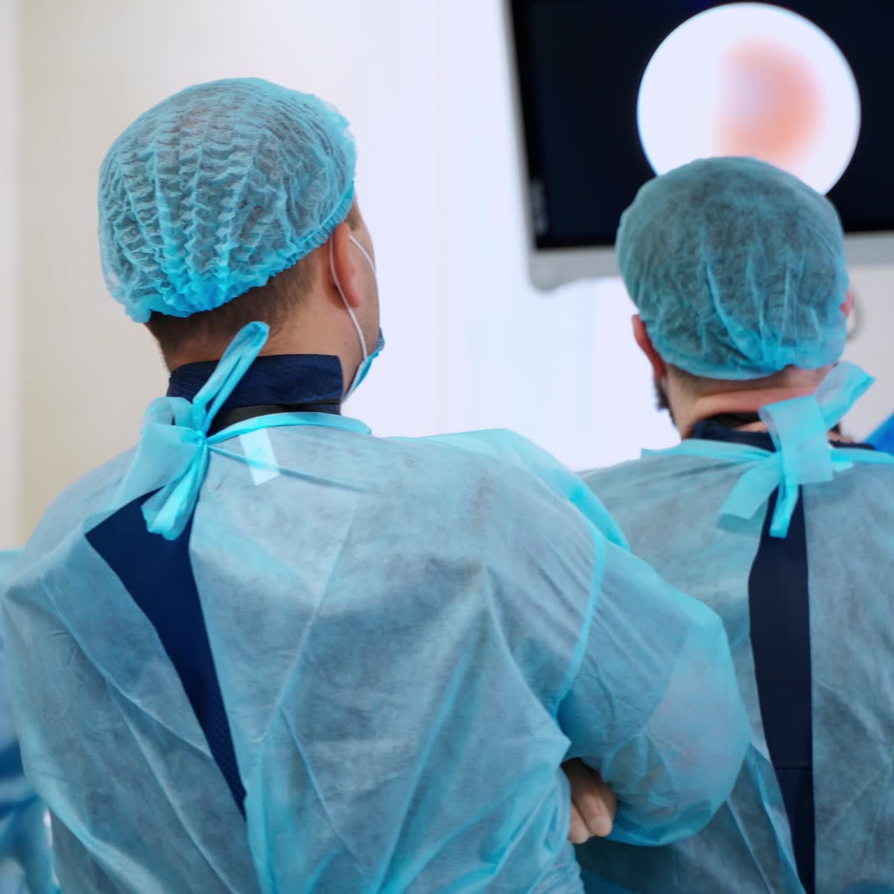 Doctors look on monitor in the operating room. Back view of medical workers during surgery. Laparoscopic operation in clinic.