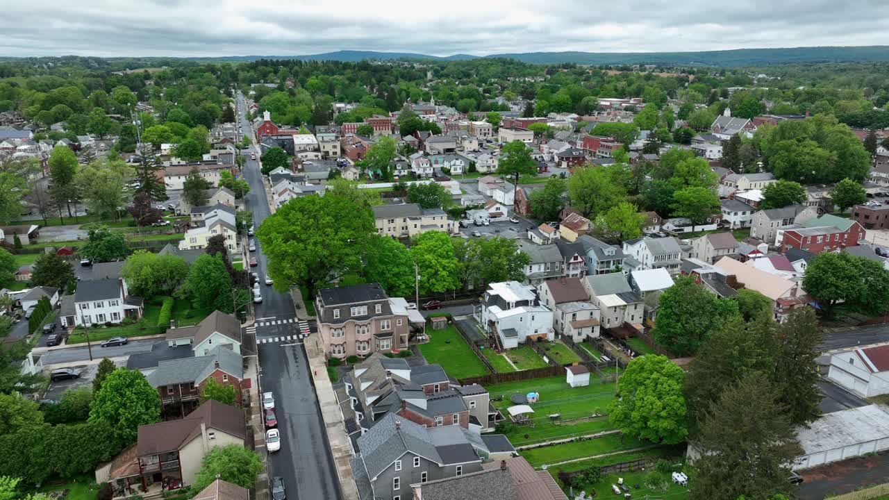 Colonial and Victorian houses and homes in small american town with green trees. Overcast clouds in sporing season. Descend drone wilde shot. American housing area with row of buildings.