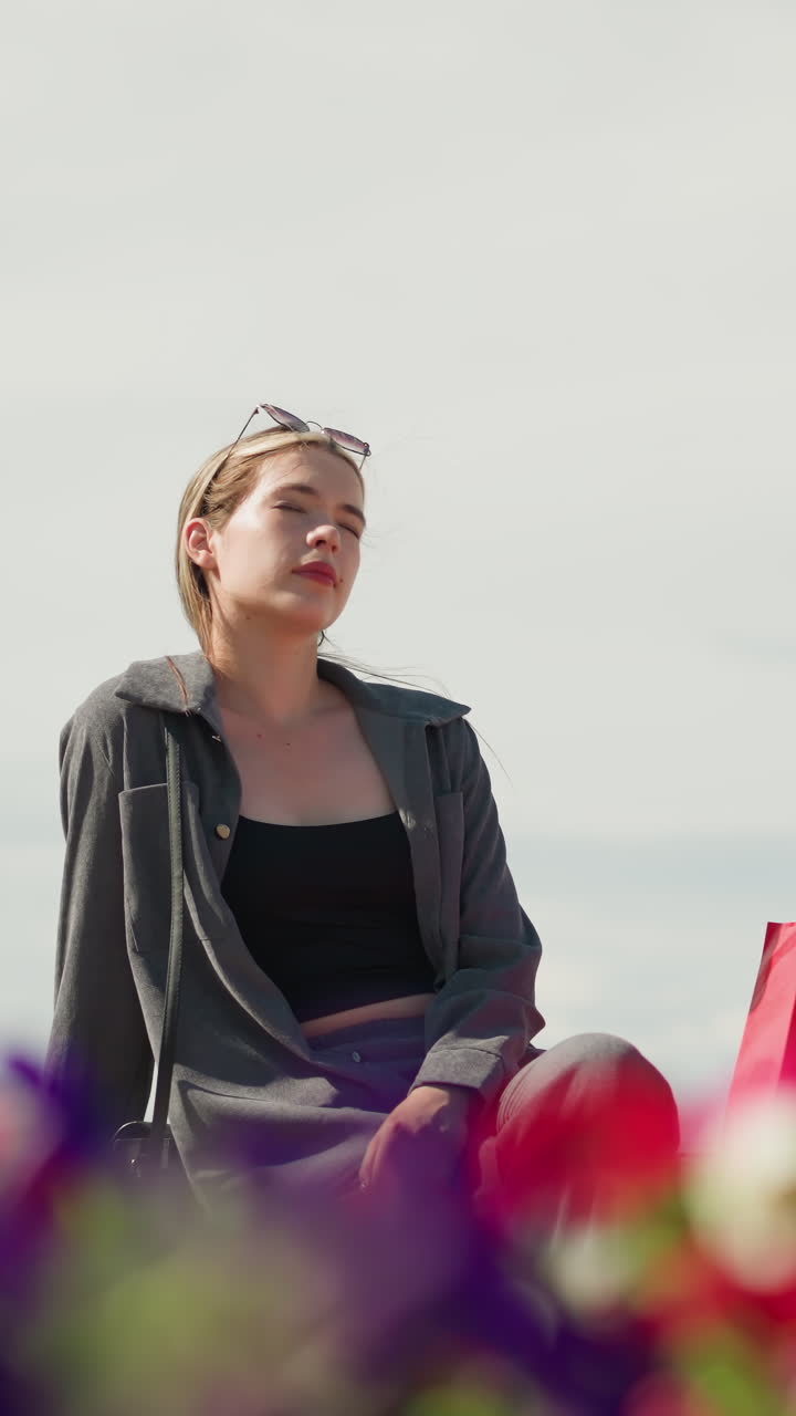 la señora coloca sus bolsas de compras en un banco, se sienta, y relaja su mano izquierda mientras la luz del sol se refleja en su cara, en el fondo borroso, un ciclista pasa como una lámpara de calle es visible