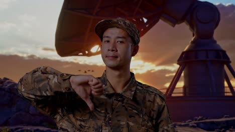 close up of asian man soldier showing thumbs down gesture to camera while standing with satellite dish