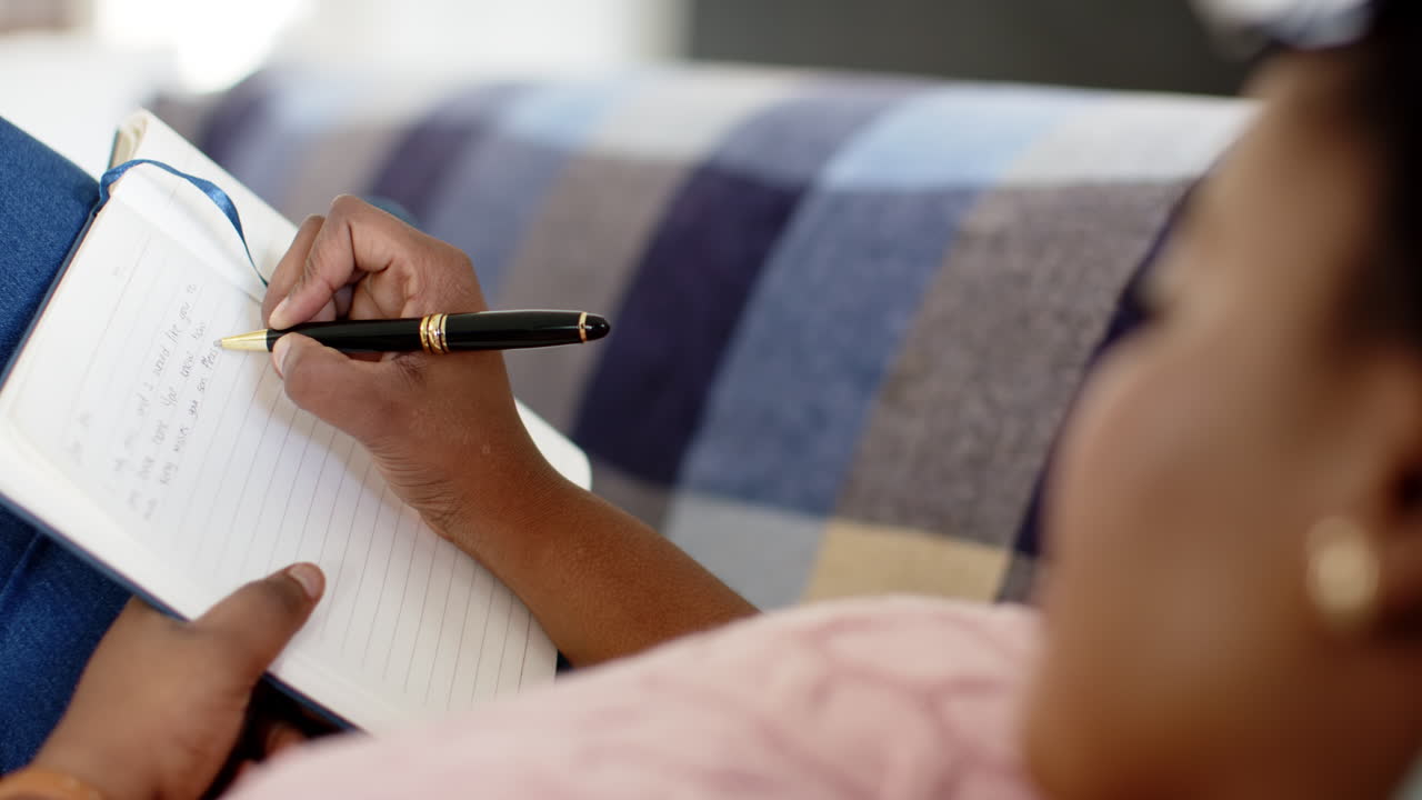 Una donna afroamericana scrive su un quaderno, seduta su un divano a casa.