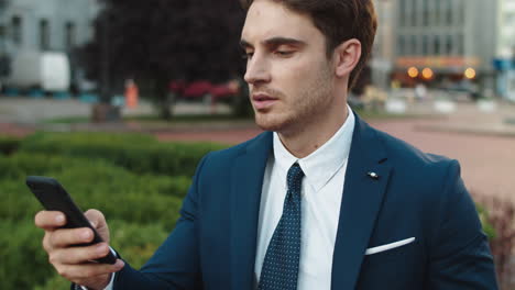Portrait-of-elegant-business-man-writing-message-on-smartphone-in-street.